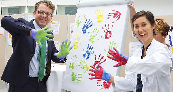 Mit bunten Farben testen Geschäftsführer Nicolas von Oppen und Apothekerin Paola Rosa Maran, ob sie die Handschuhe ohne Hautkontakt ausziehen können. Foto: Klinikum Landshut