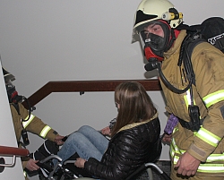Evakuierung einer Rollstuhlfahrerin mit Einsatz von Atemschutzgeräten.